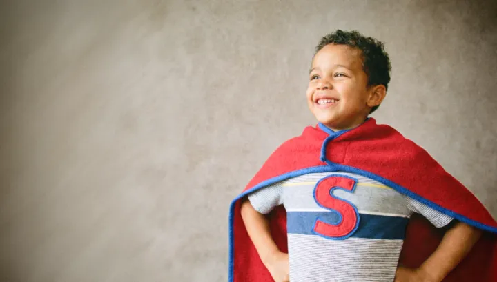 Un enfant se tenant droit et souriant. il regarde au loin et porte une cape faite d'une couvertur